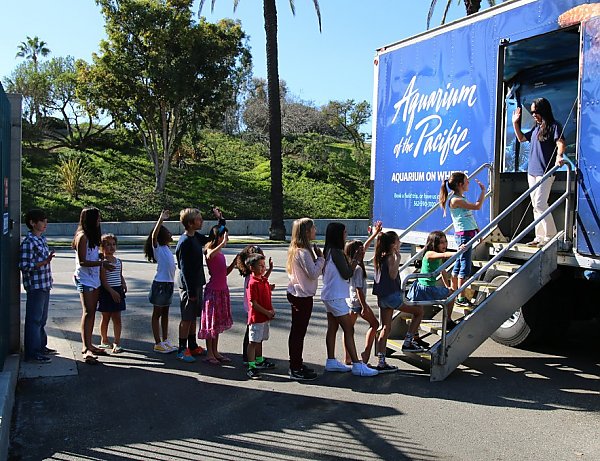 About a dozen children form a line outside the Aquarium on Wheels box truck while an educator welcomes them in from the top of the stairs.