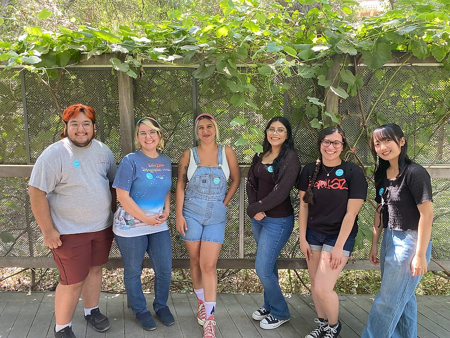 Six people smiling while standing shoulder to shoulder outside